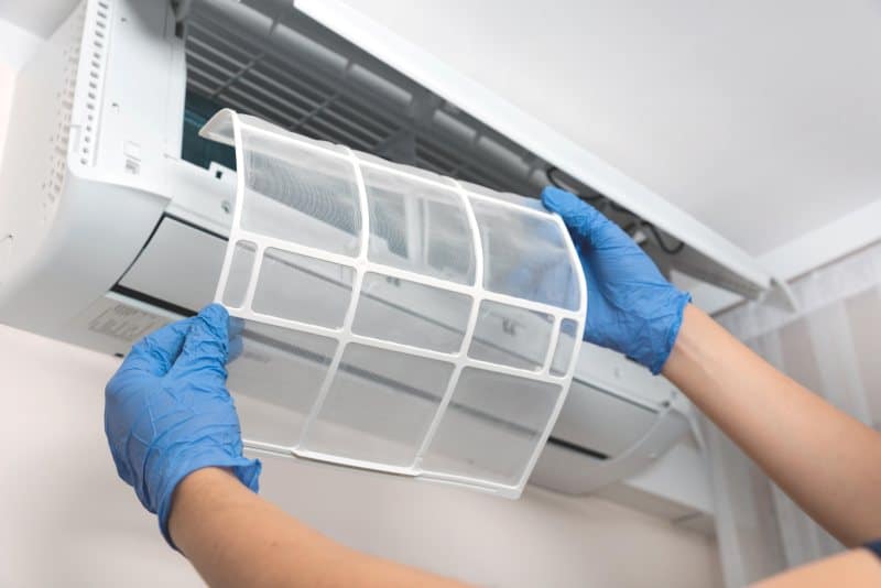 A person removing an air conditioner filter for cleaning, maintaining the AC system to ensure optimal cooling efficiency.