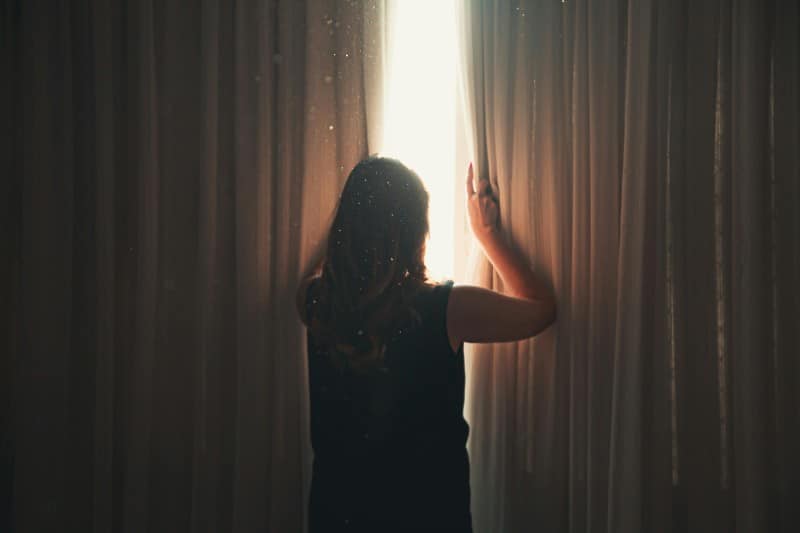 A person adjusting curtains to let sunlight in, indicating the need for better airflow to cool the room.