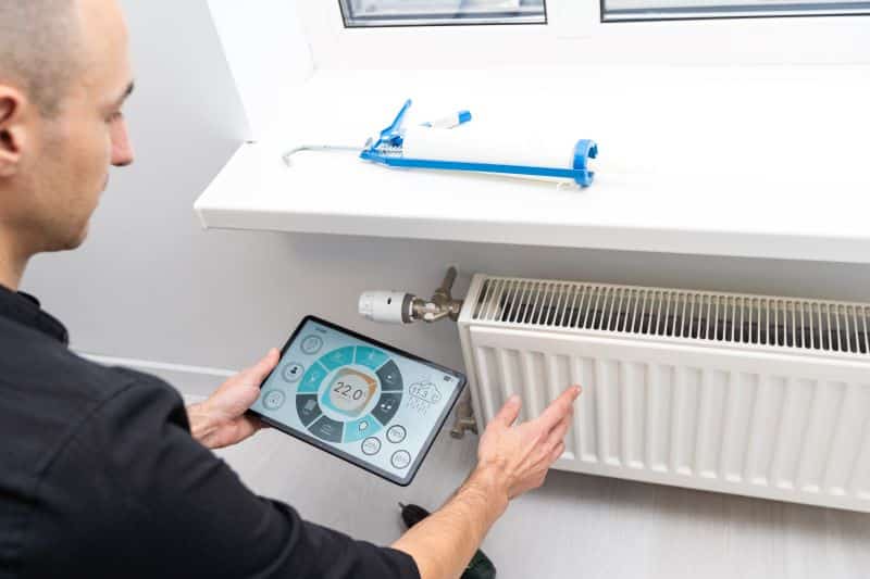 A person adjusting the temperature of a radiator using a tablet, optimizing the home heating system.