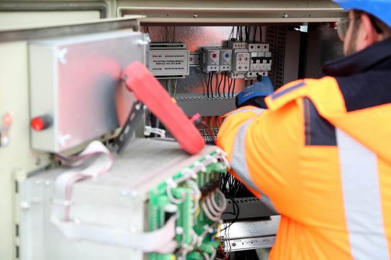 An electrician in safety gear working on wiring inside an electrical panel, showcasing the task of industrial electricians.