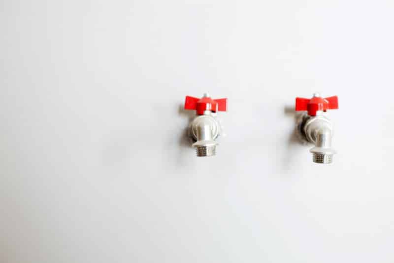 Close-up of two faucets with red handles mounted on a white wall, representing common plumbing fixtures that may be involved in typical plumbing mistakes.