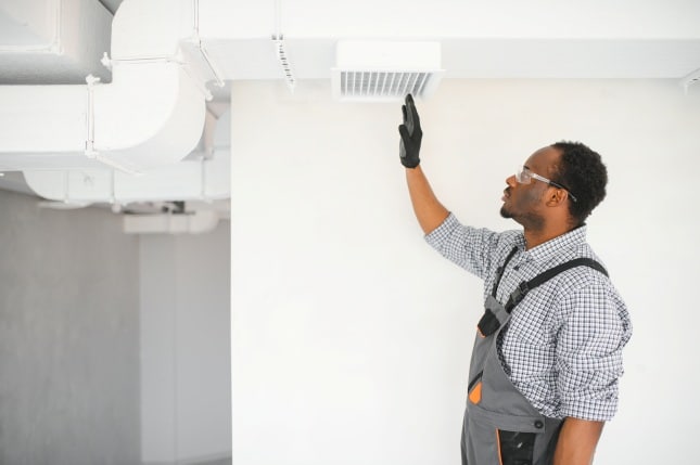 Person adjusting an air vent in a commercial building while wearing safety gloves and glasses.
