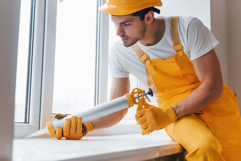 Worker applying professional caulking around a window frame, ensuring a tight seal to extend the life of the window and building materials.