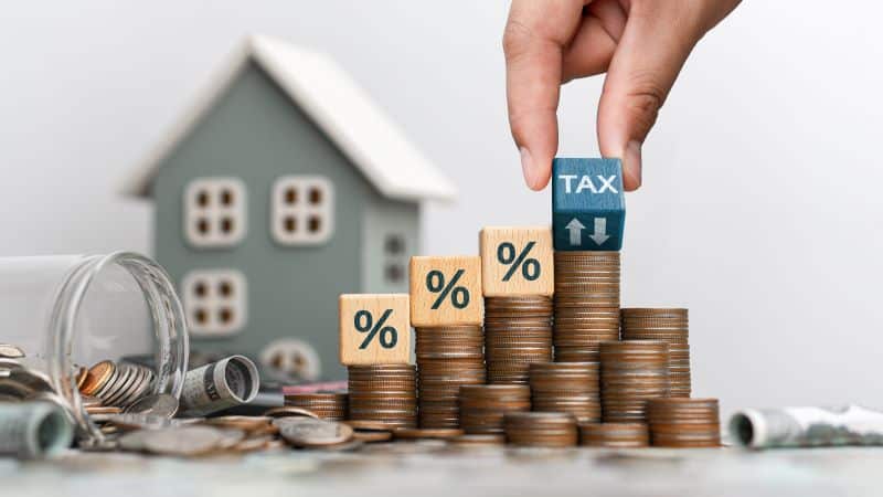 Stacked coins with tax and percentage blocks, symbolizing the tax strategies for real estate investors to minimize their liability and maximize profits.