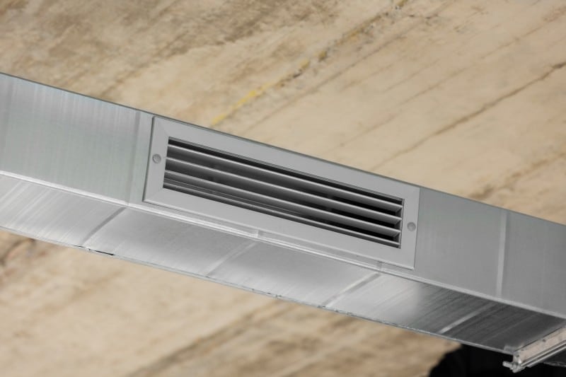 A close-up view of a metallic air ventilation duct with horizontal slats installed on the ceiling, providing airflow in a building.