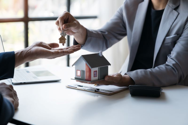 A real estate transaction where a person is handing over the keys to another, with a small model house placed on the table, symbolizing the process of selling your home.