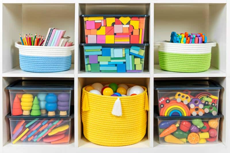 Colorful home storage ideas using labeled clear bins and woven baskets to organize children's toys, blocks, and art supplies in a cubby shelf.
