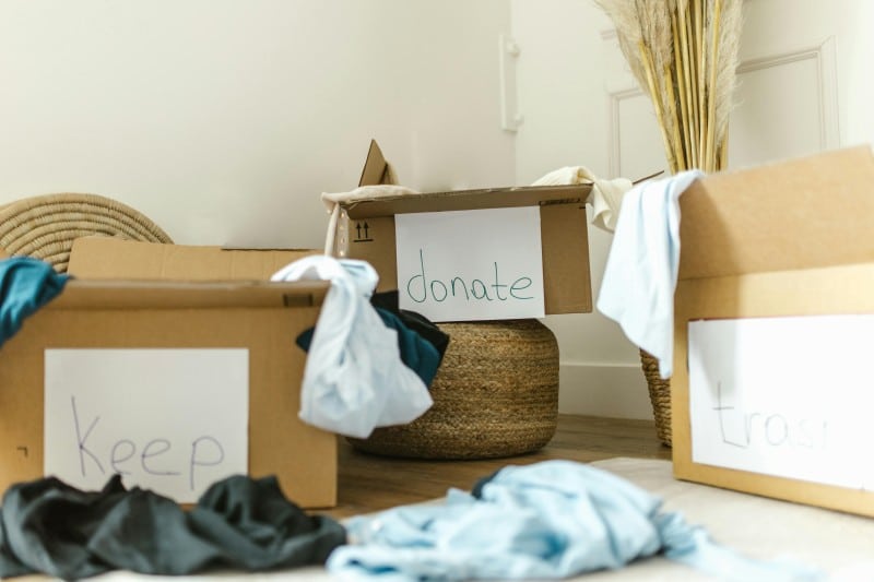 Cardboard boxes labeled keep, donate, and trash filled with clothes, used for decluttering before changing weather seasons.