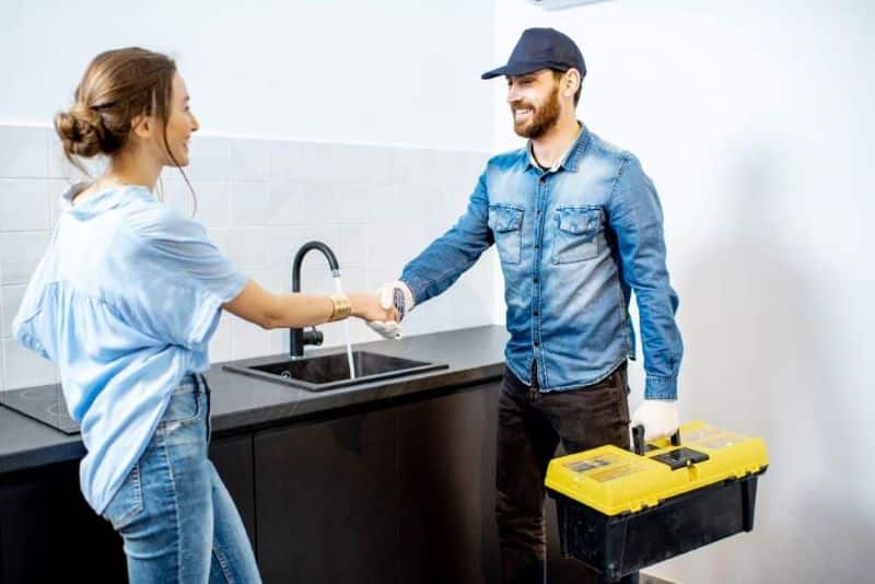 A professional plumber shaking hands with a customer after providing drain cleaning services in a kitchen.