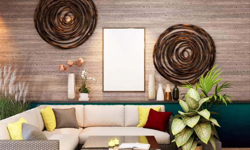 A cozy living room featuring a beige sofa with colorful cushions, surrounded by plants and decorative vases. The wooden wall is adorned with circular wall art, and there is a blank frame hanging above the sofa. A modern, natural-themed interior decor design.
