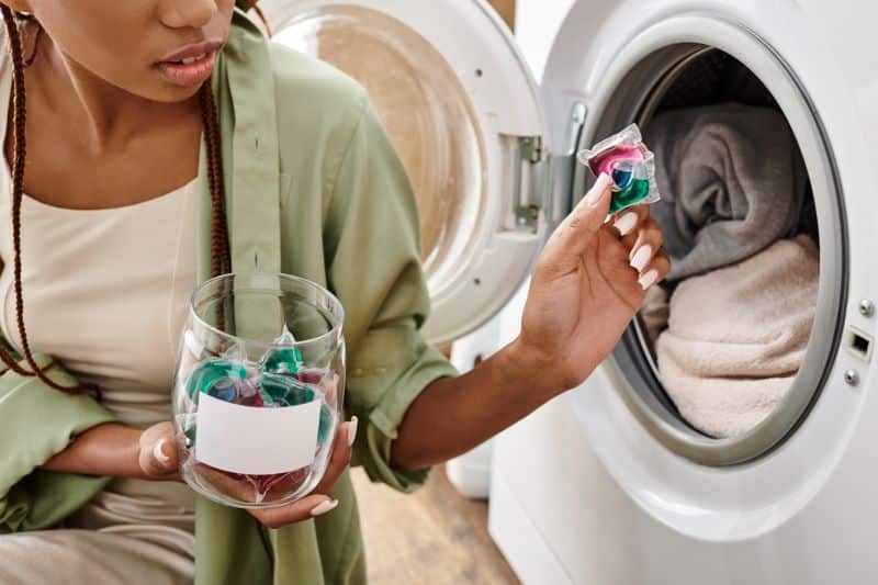A woman holding a jar of laundry pods, while preparing to add one into a washing machine with a load of laundry inside.