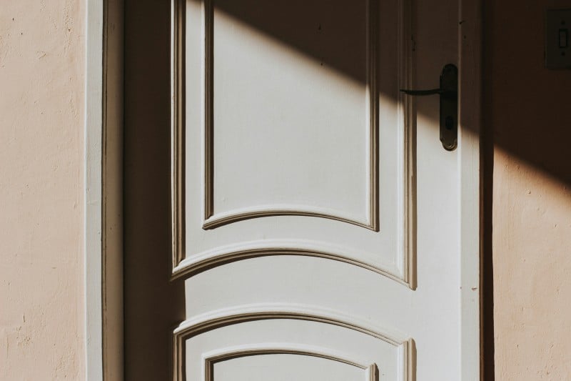 Sunlight casting shadows on a closed white wooden door, showing how design choices can affect natural light flow indoors.