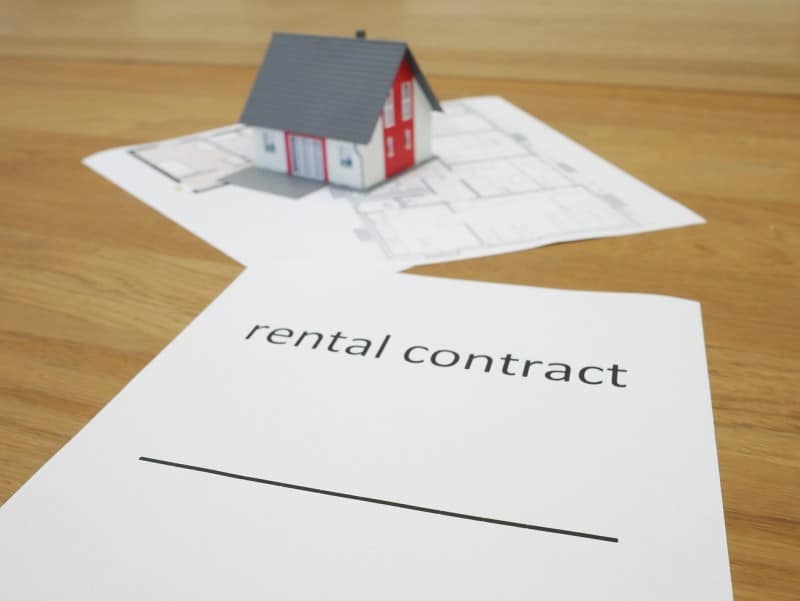 Rental contract document and house floor plans with a small model home on top, representing home fixes and property value enhancement.