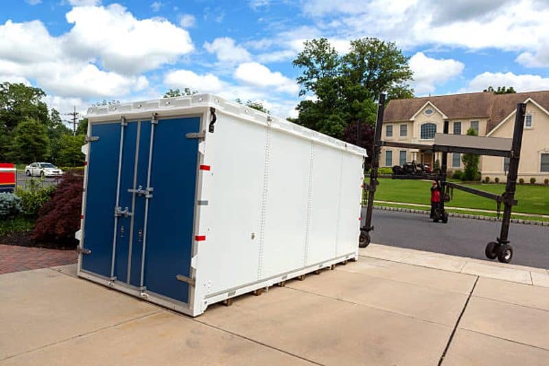 Portable storage container placed in a driveway to keep items safe and out of the way while repairing your house.