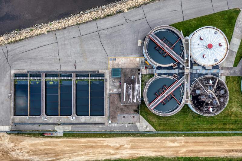 Aerial view of a wastewater treatment facility showing multiple round clarifier systems and rectangular sedimentation tanks designed for modern wastewater management.