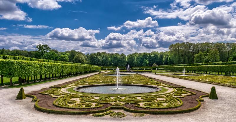 Formal garden with trimmed hedges, patterned topiary, and central fountain under a partly cloudy sky — ideal inspiration to revamp your garden layout.