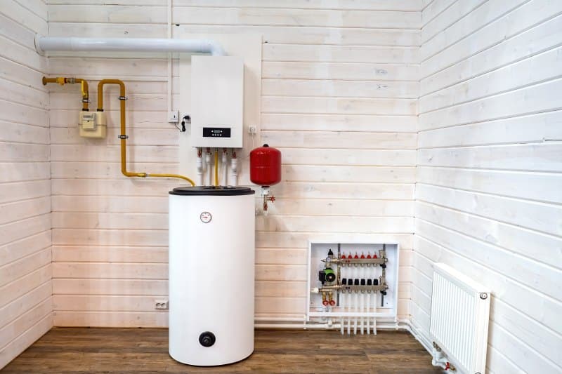 Modern hot water system installed in a wooden-paneled utility room, showing storage tank, boiler, and connected heating pipes.