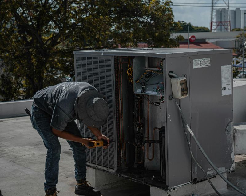 Technician performing preventative HVAC maintenance by inspecting and repairing a rooftop air conditioning unit to improve energy efficiency.