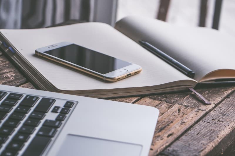 Smartphone, notebook, pen, and laptop on wooden desk representing a digital workspace setup for a home business.
