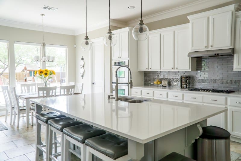 Modern white kitchen with island, pendant lights, and dining space showing key mistakes to avoid in home updates.