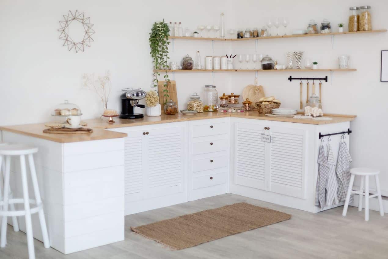 White minimalist kitchen with wooden countertops, open shelves, and organized storage jars.
