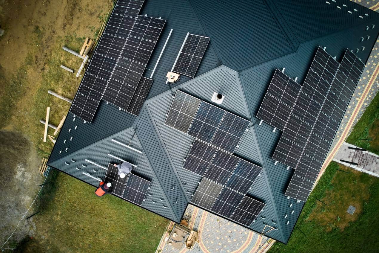 Aerial view of workers installing multiple solar panels on a modern house roof for energy storage and solar power generation.