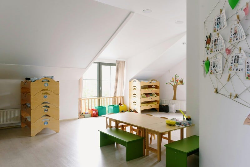 Bright and organized kids’ playroom with wooden bunk storage units, green benches, and a central table, maximizing storage space under sloped ceilings.