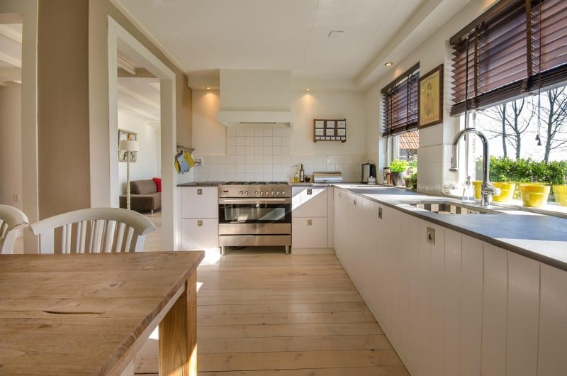 Open-concept kitchen with white cabinets, wooden dining table, large windows, and stainless steel oven; bright and modern concept kitchen.