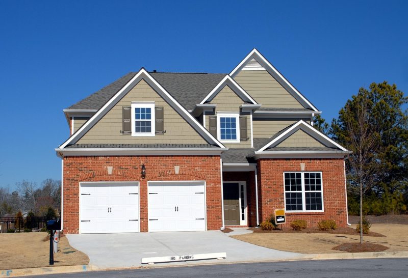 A modern two-story suburban house with a double garage featuring white garage doors, a brick and siding exterior, and a clean driveway, illustrating contemporary garage designs.