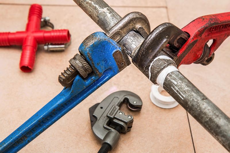 Two pipe wrenches tightening a metal pipe with sealing tape, surrounded by plumbing tools, showing professional plumbing service work.