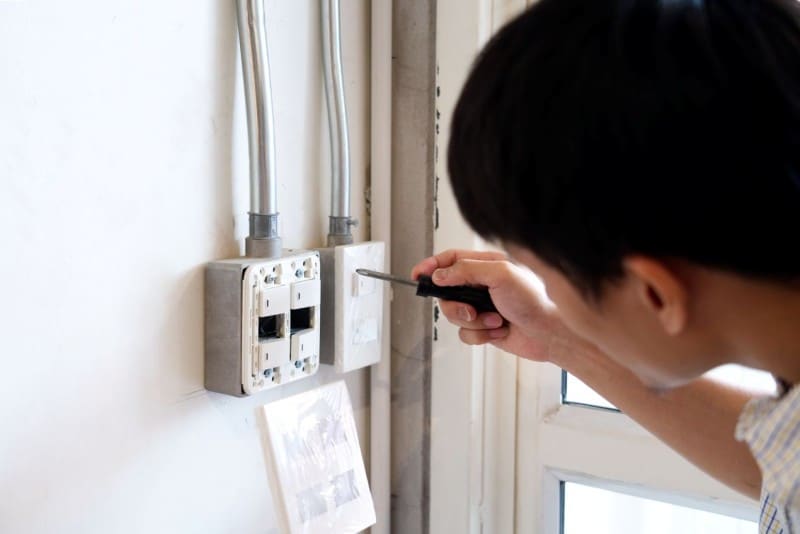 Person using a screwdriver to repair or install an electrical outlet box on the wall, an essential step during a power outage.