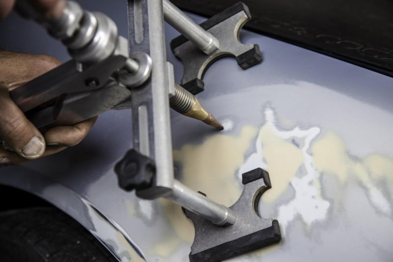 Close-up of a mechanic using a dent puller tool on a car panel, showing the process of professional auto body repair.
