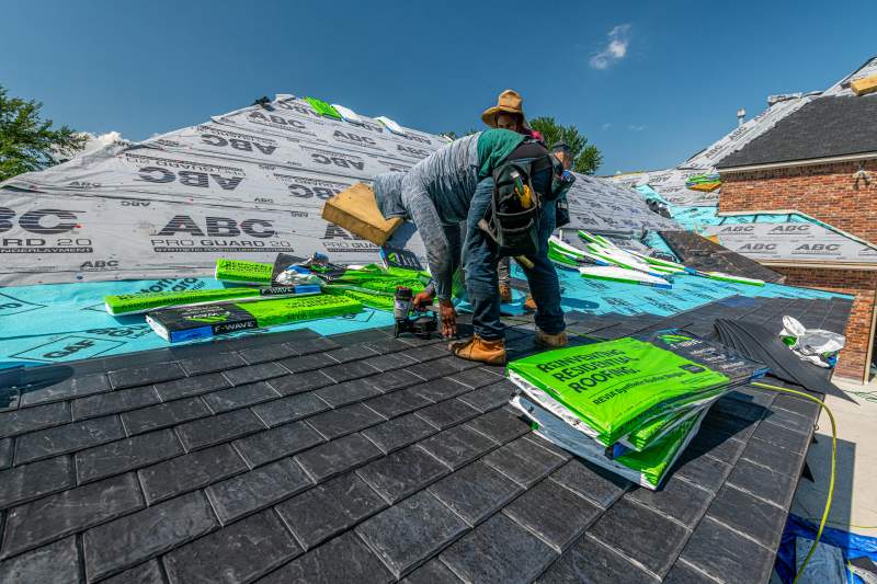 Roofing contractors working on roof installation, checking underlayment and shingles for wind damage during inspection.