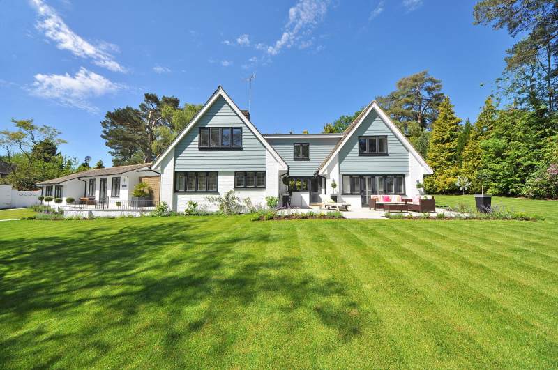 Modern house with large green lawn and trees in the background, illustrating a home prepared for seasonal changes.