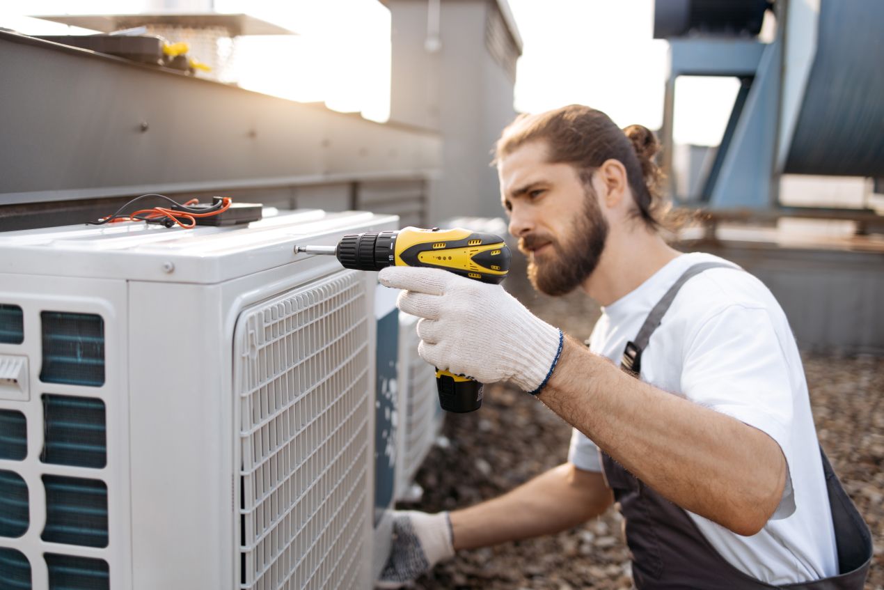 Professional AC repair worker using a drill to service an outdoor air conditioning unit, ensuring reliable cooling and reduced energy costs.