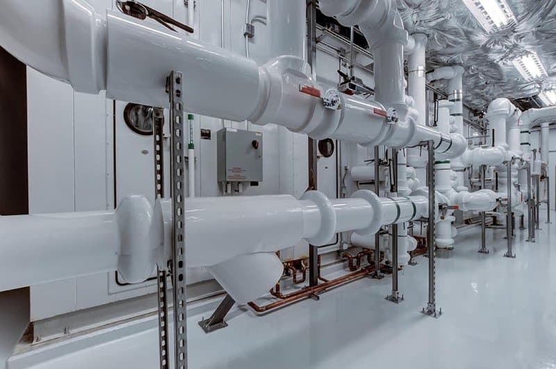 Industrial mechanical room with large white insulated commercial plumbing pipes, valves, and metal supports, showcasing a clean and organized plumbing system — ideal example of professional commercial plumbing maintenance in Victorville.
