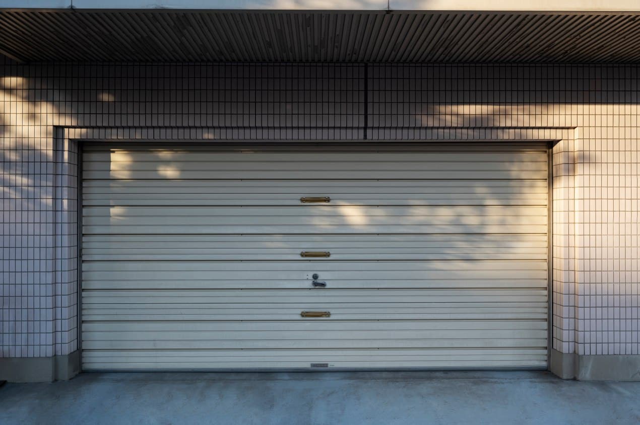 Closed white metal garage door on a tiled exterior wall, showing handles and a lock in the center; suitable for articles about why a garage door is not closing all the way.