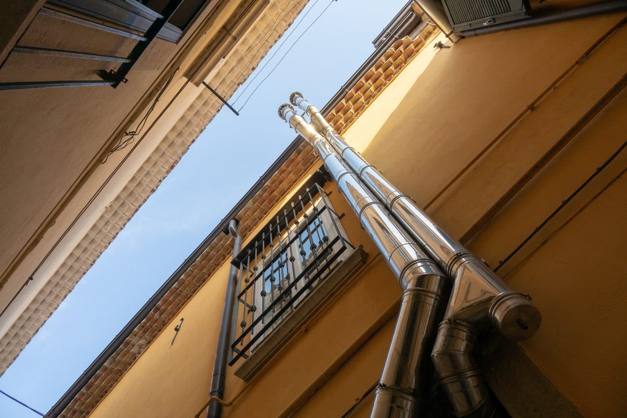 Upward view of metal drainage pipes on a yellow building wall, showing gutter work done by professionals.