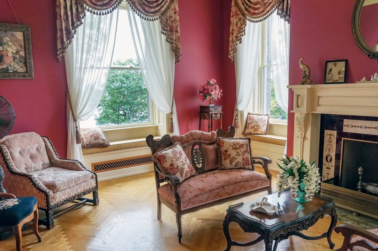 Elegant vintage living room with red walls, ornate curtains, floral-patterned furniture, and classic fireplace; showcases timeless home decor style with antique touches and warm lighting.