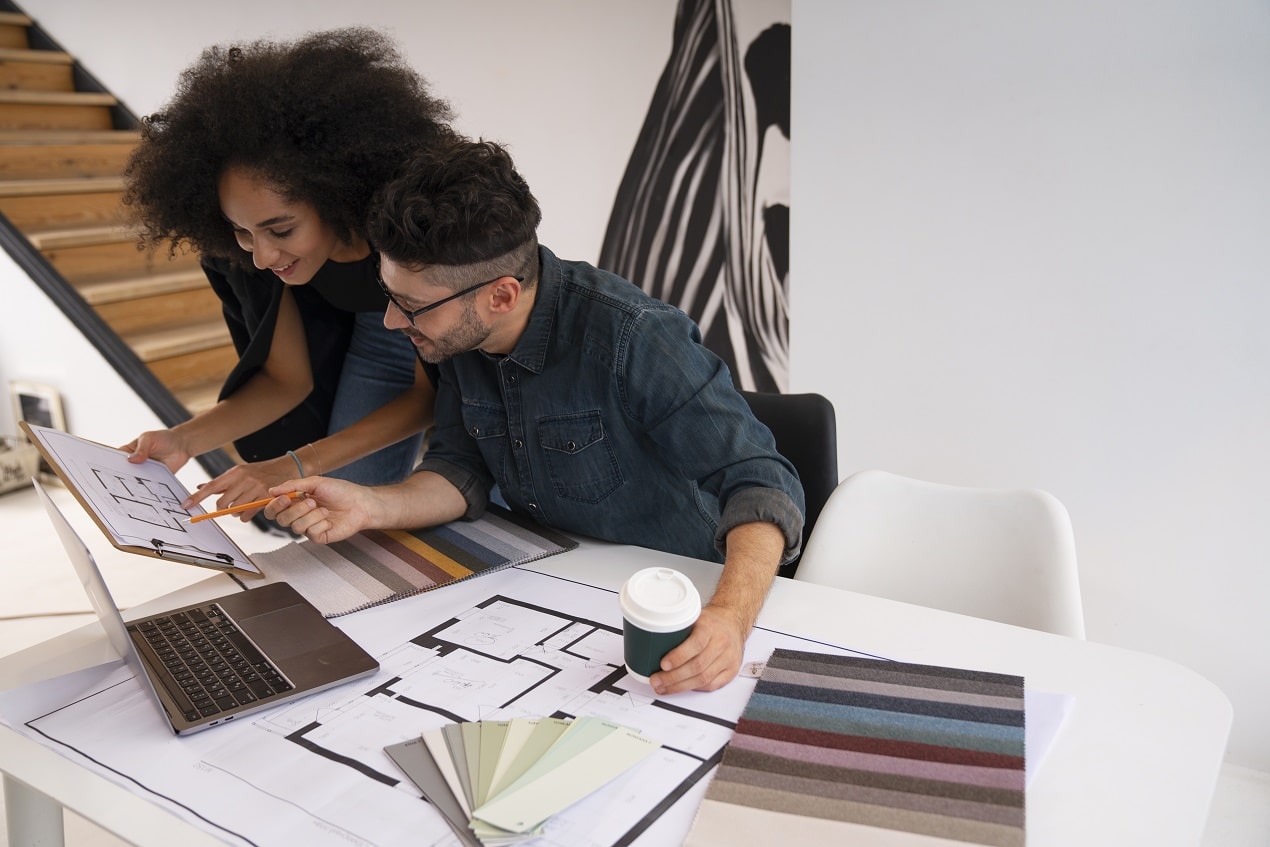 Two interior architects reviewing building floor plans and color swatches at a desk, discussing design choices for multi-functional work zones.
