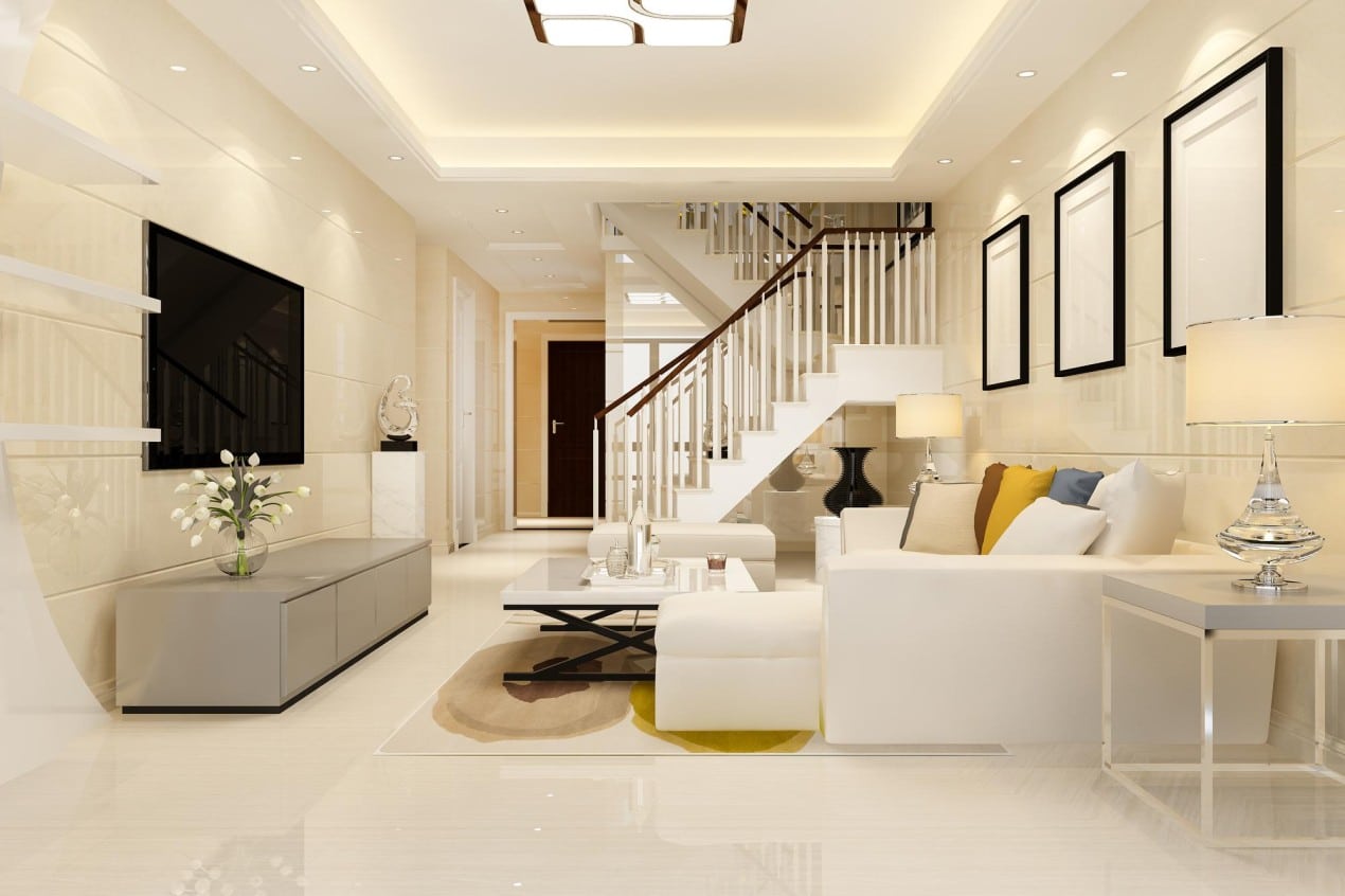 Modern living room interior featuring sleek white furniture, a glass coffee table, decorative pillows, a flat-screen TV, and a contemporary staircase with wooden handrails. The bright lighting and minimalist design highlight a modern home aesthetic.