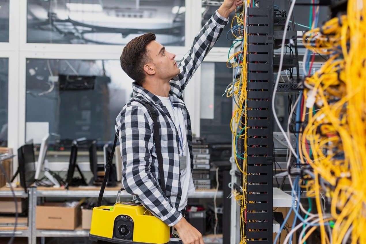 Technician organizing colorful network cables in a server room while carrying AV installation equipment.