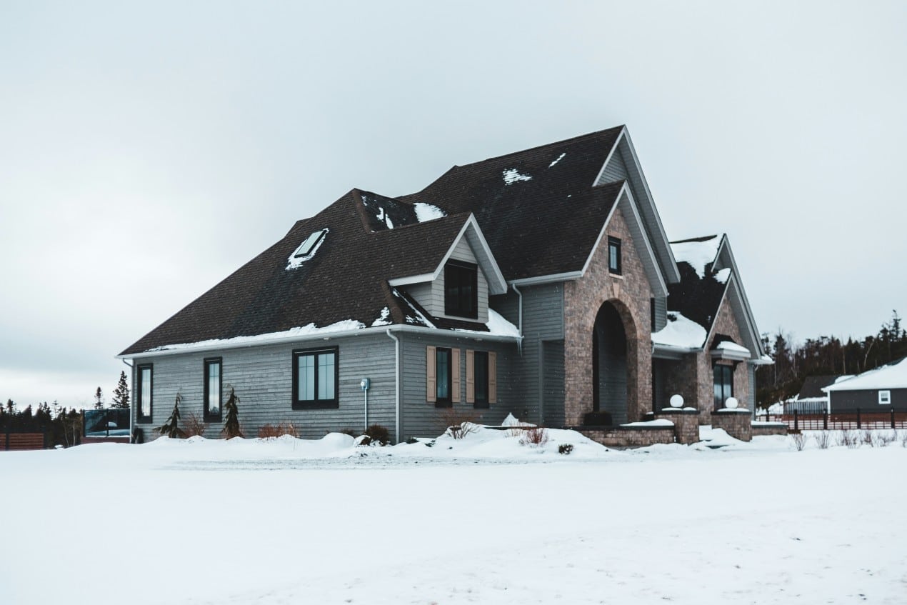 Modern new build house with gray siding and brick entryway surrounded by snow, showing what to expect during the first winter in a new build.