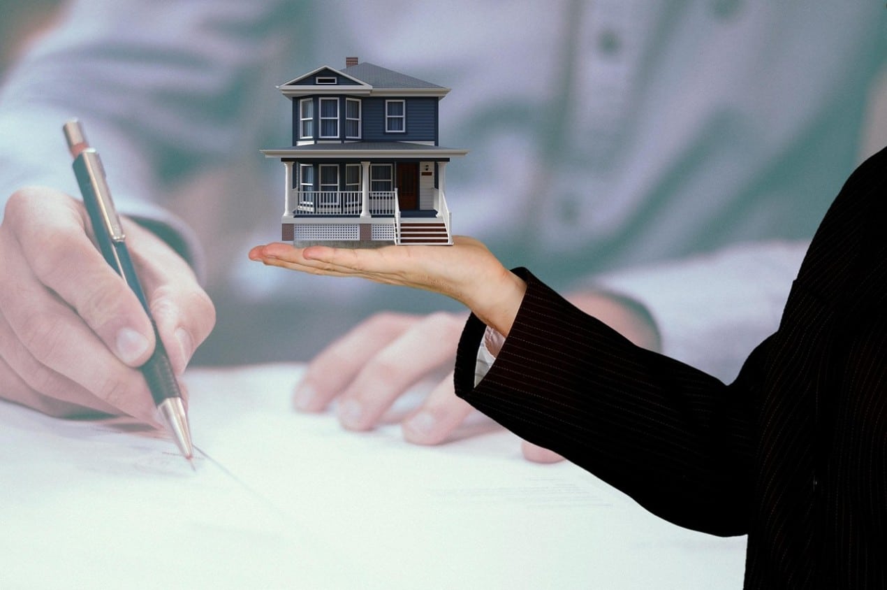 A person holds a small house model, symbolizing property ownership and real estate agreement.