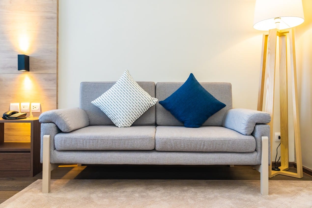 Modern gray sofa bed with two cushions beside a wooden lamp, showing a stylish and space-saving design.