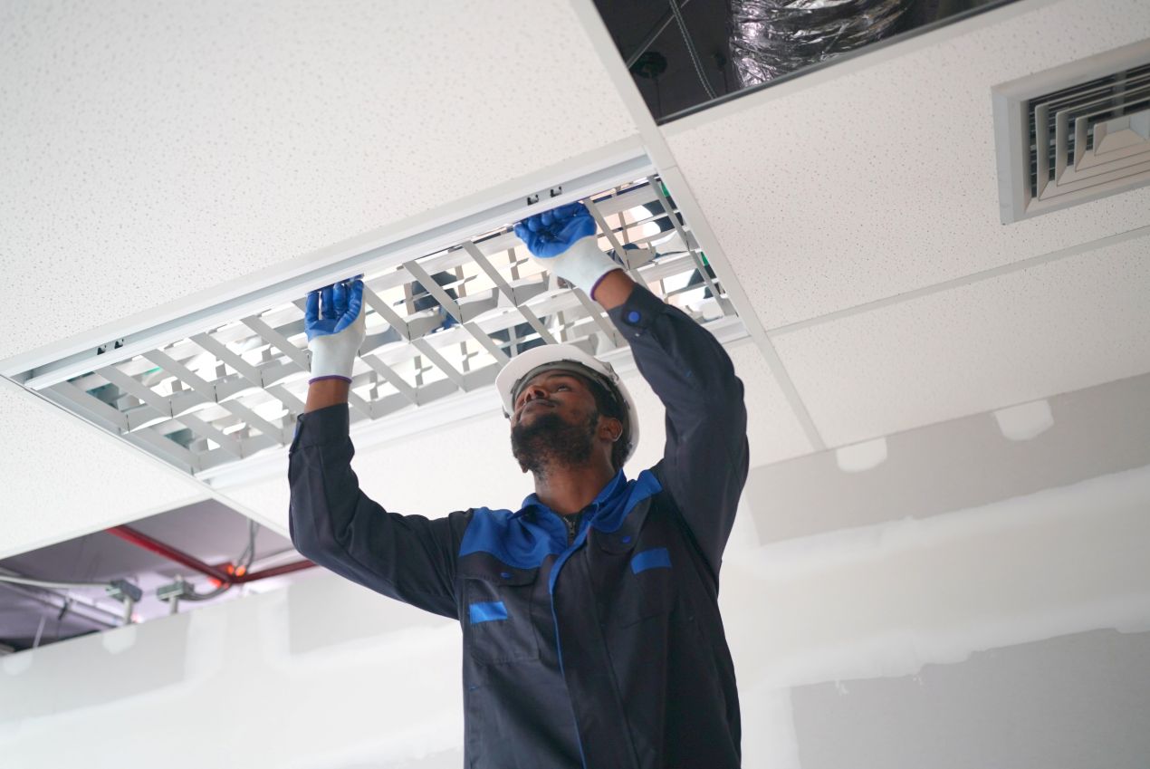 A technician installing suspended ceiling panels to reduce noise and provide easy access to electrical and HVAC systems in a modern building.