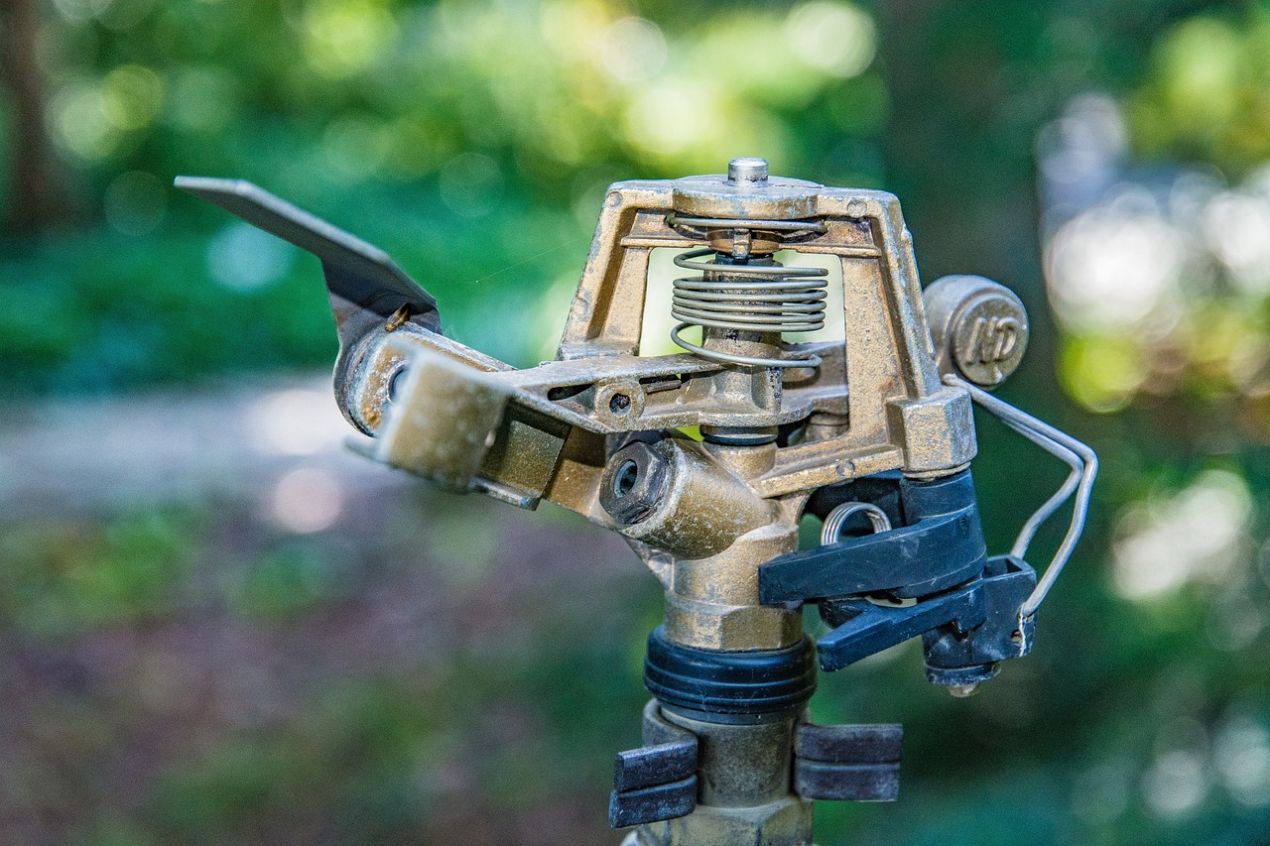 Close-up of a brass garden sprinkler head with metal spring and rotating arm used for lawn irrigation, illustrating proper sprinkler repair and maintenance to save water and money.