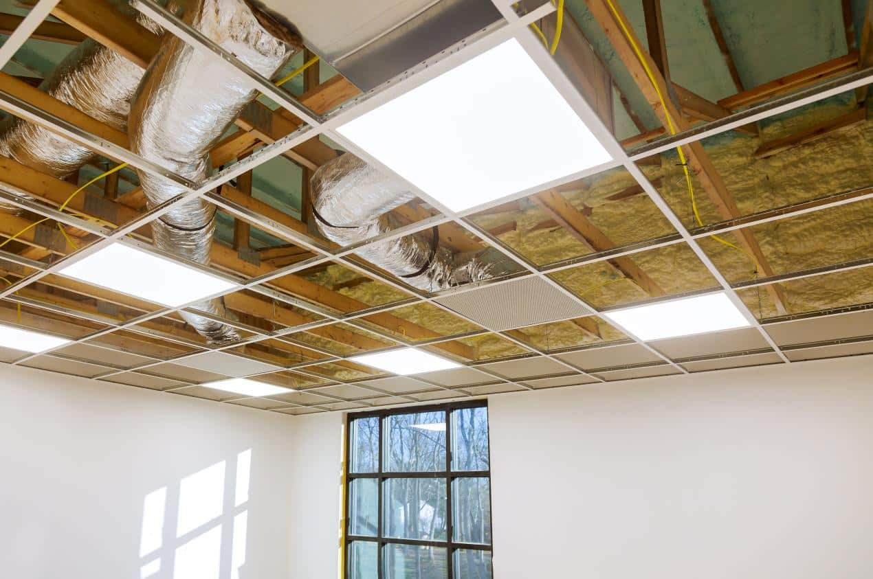 A suspended ceiling framework showing insulation, lighting panels, and ductwork for noise reduction and efficient wire management.