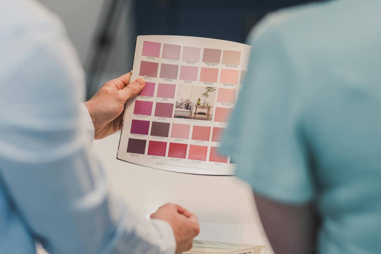 Two people reviewing a color palette book with various pink shades, possibly discussing paint options for a home renovation project using a bridge loan.