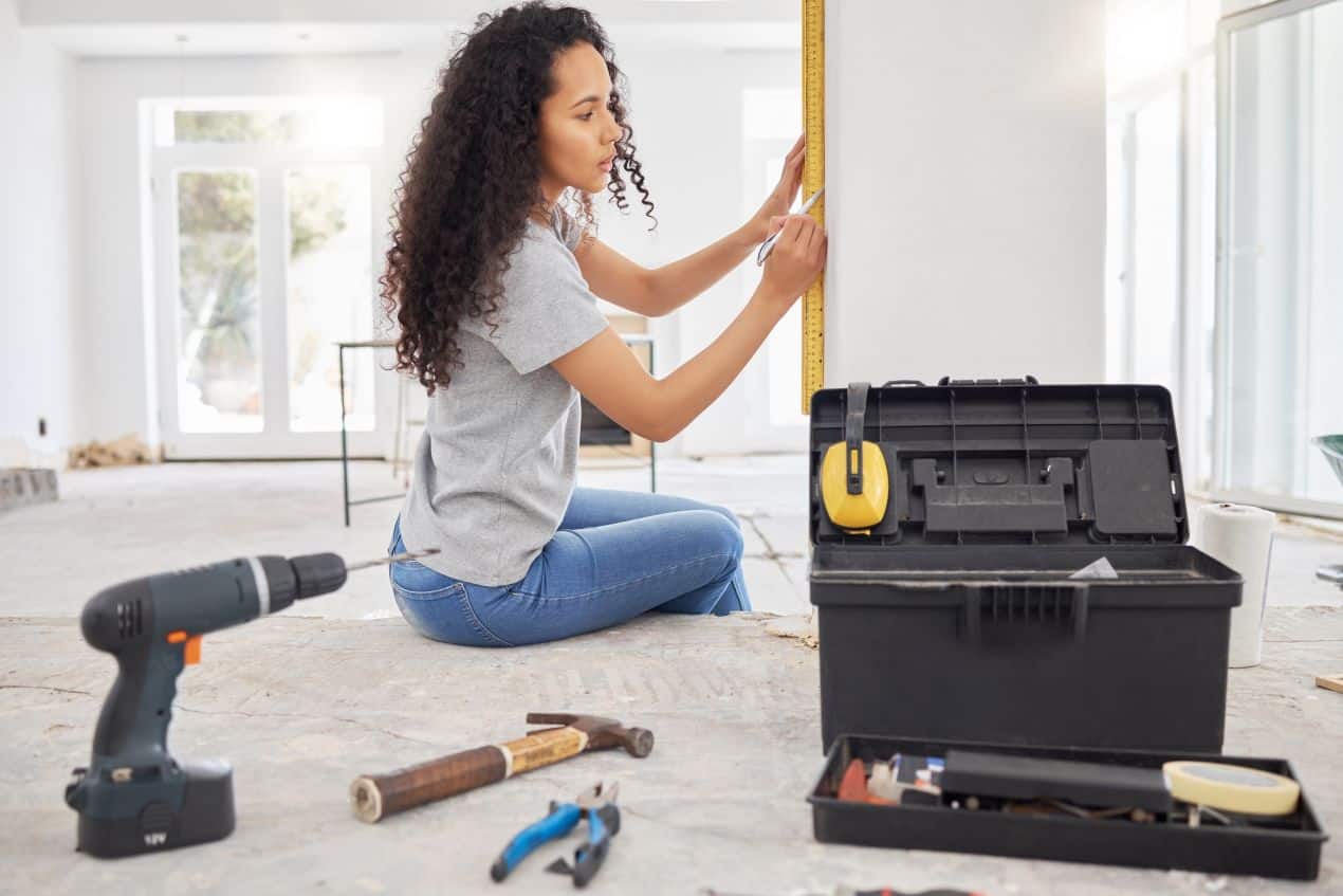 Woman measuring and marking a wall during small home repairs, surrounded by basic tools.